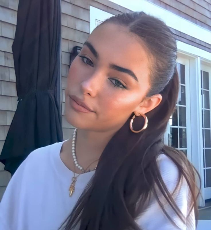 a woman with long hair wearing large gold hoop earrings and a white t - shirt