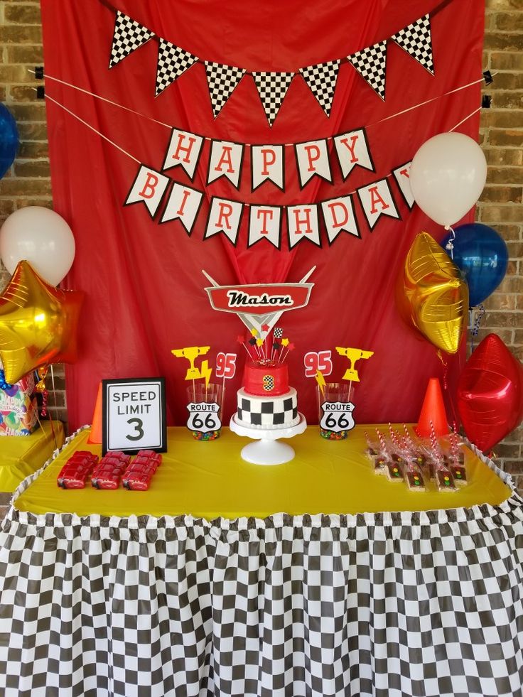 a birthday party with balloons, cake and race car decorations on a table in front of a red backdrop