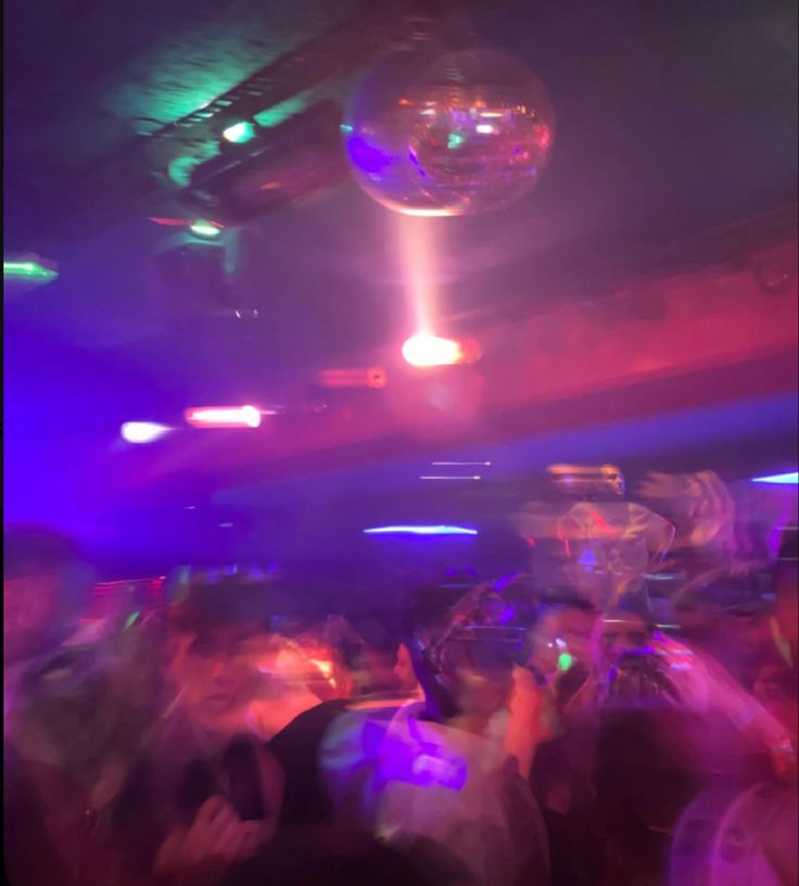 a group of people are dancing in a club with disco balls hanging from the ceiling