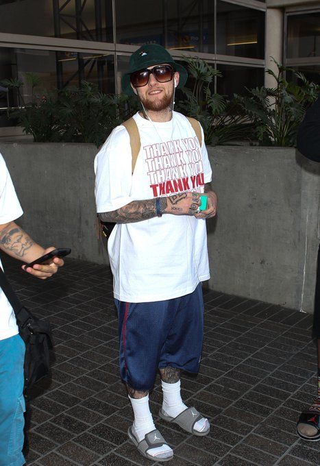 a man in white shirt and blue shorts standing next to another man with tattoos on his arm