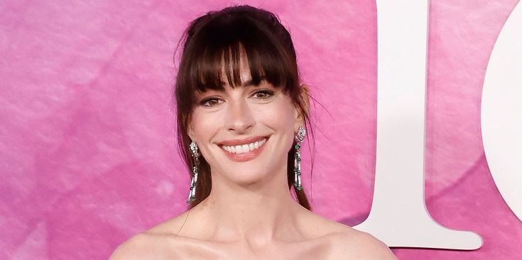 a woman in a strapless dress smiling at the camera with her hair pulled back