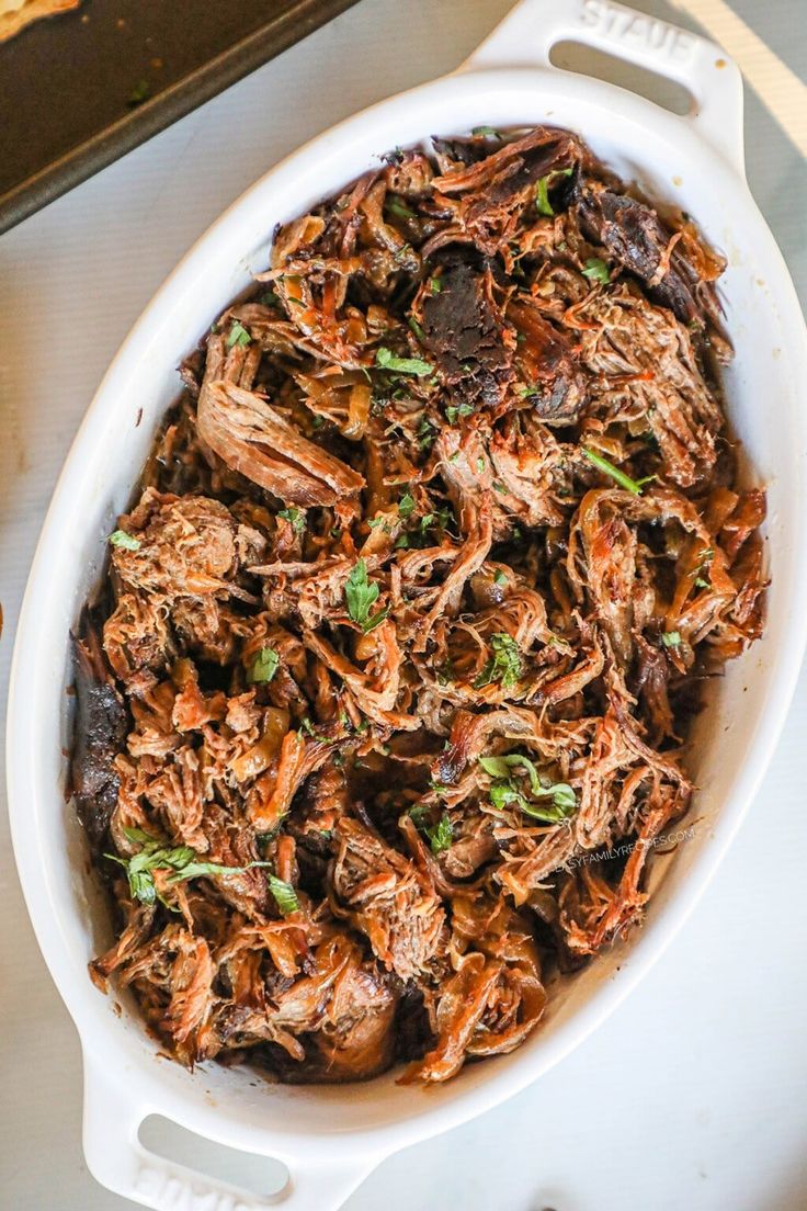 a white casserole dish filled with pulled pork and mushrooms, garnished with parsley