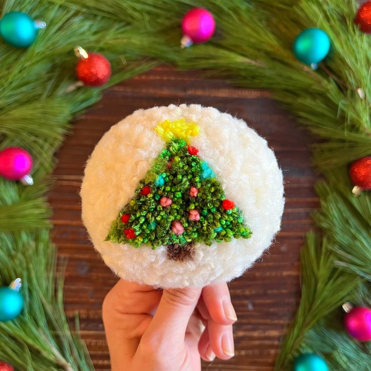 someone is holding up a small christmas ornament in front of a wreath with ornaments around it