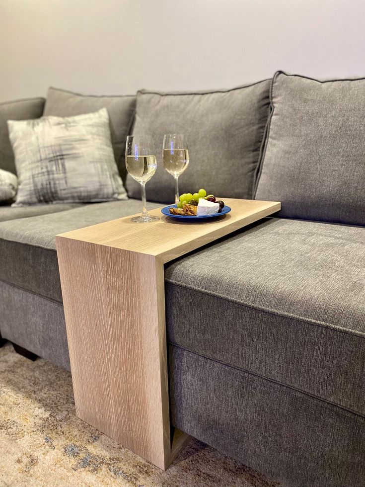 a table with two glasses of wine on top of it next to a gray couch