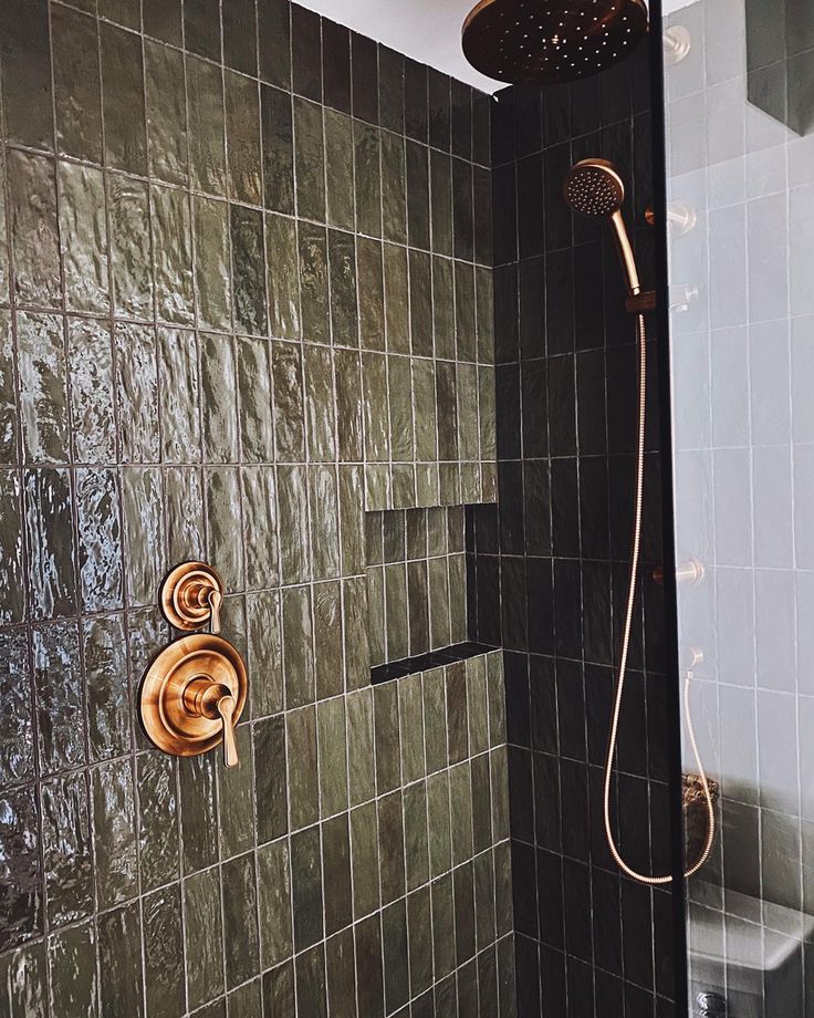 a shower head and hand shower in a bathroom with green tiles on the walls, along with a gold faucet