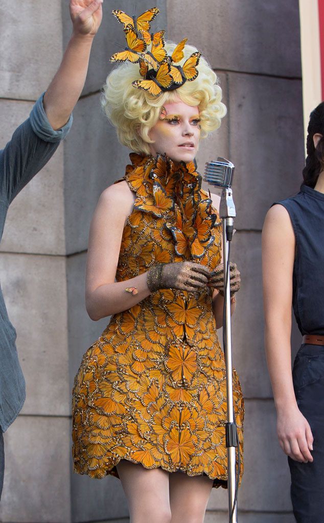 a woman in a yellow dress holding a microphone while standing next to a man wearing a butterfly headdress