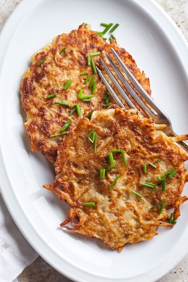 a white plate topped with two pancakes covered in cheese and green onions next to a fork