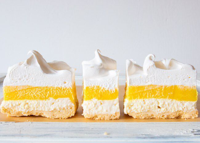 three pieces of cake sitting on top of a wooden cutting board with icing and whipped cream