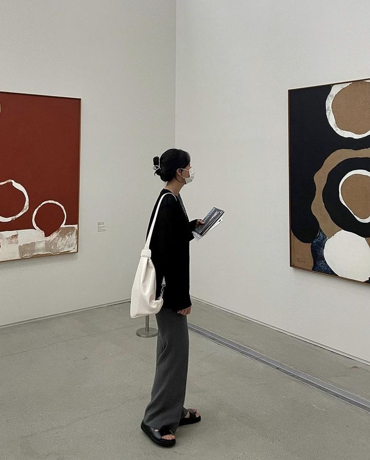 a woman standing in an art gallery looking at paintings on the wall and holding a clipboard