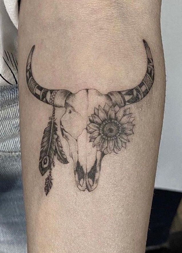 a bull's skull with flowers and feathers on the side of his leg is shown