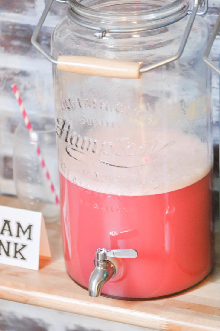 a red and pink drink in a glass jar on a wooden shelf next to a sign