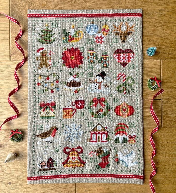 a cross - stitch christmas sample on a wooden table with red ribbon and decorations around it