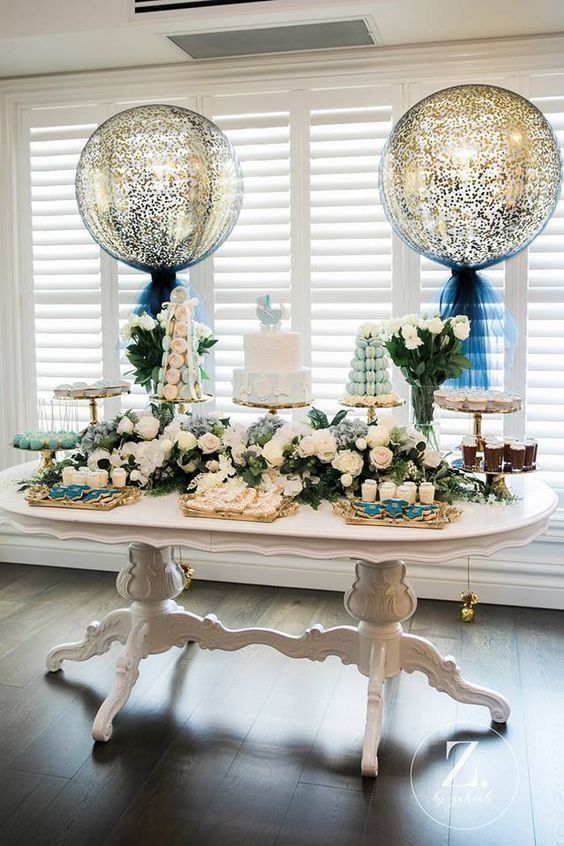 a table topped with lots of white flowers and cake next to two giant round balloons