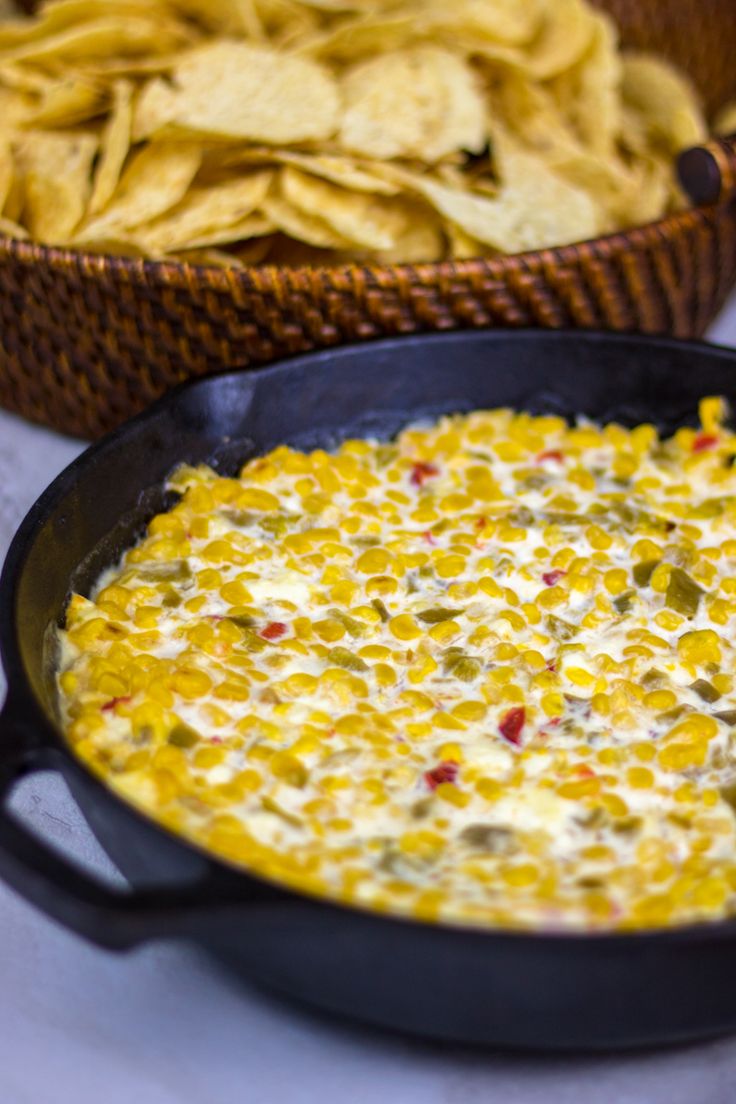 a bowl of corn dip with tortilla chips in the background