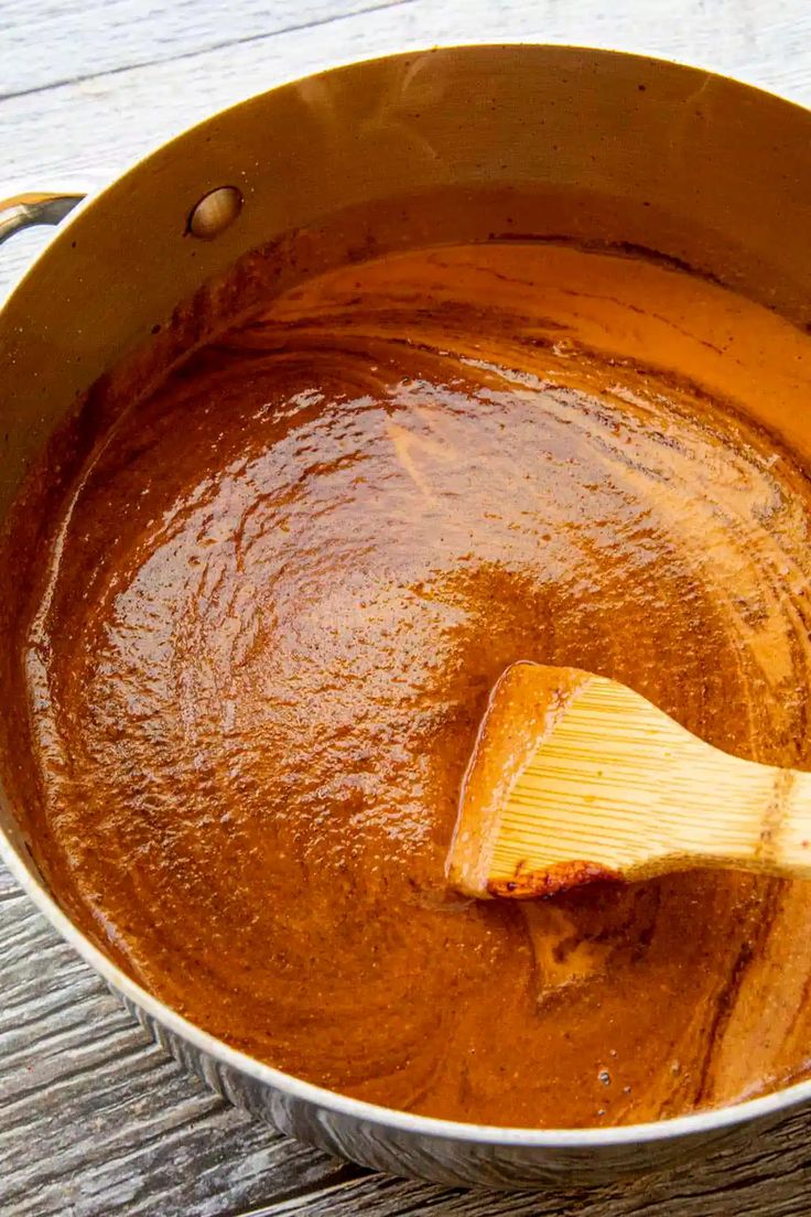 a wooden spoon in a pot filled with brown sauce on top of a wood table