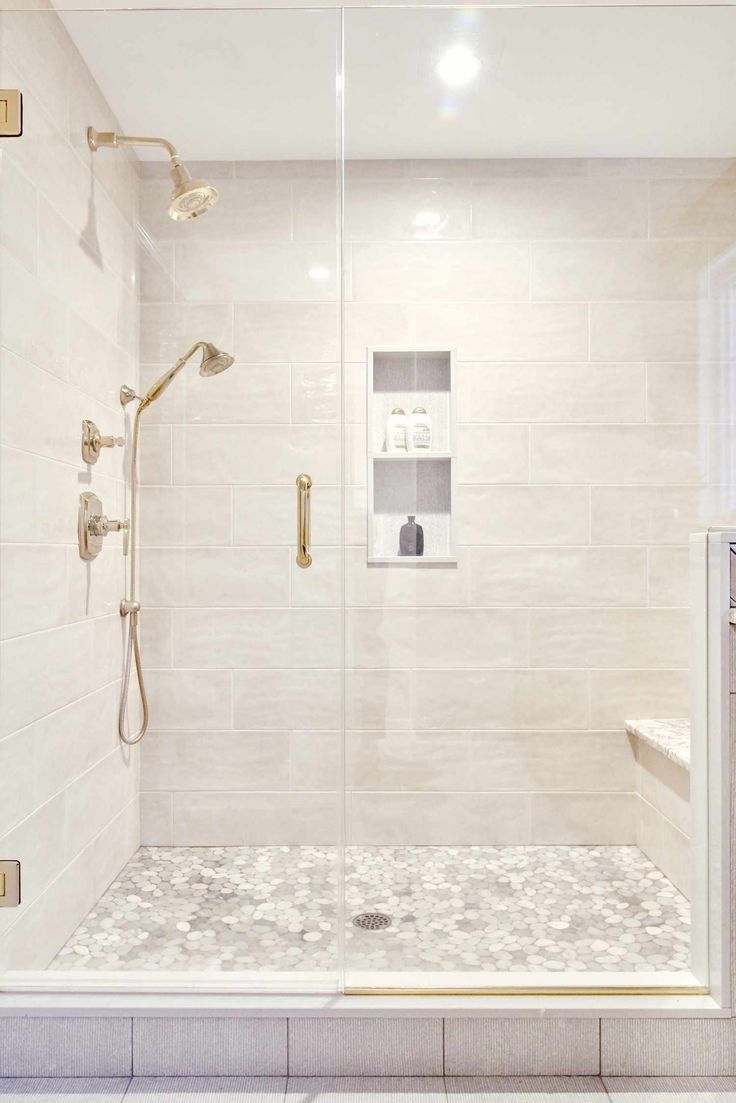 a walk in shower sitting next to a white tiled wall and floor with gold fixtures