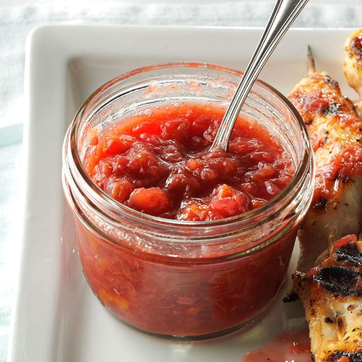 a white plate topped with chicken wings covered in ketchup next to a jar of sauce