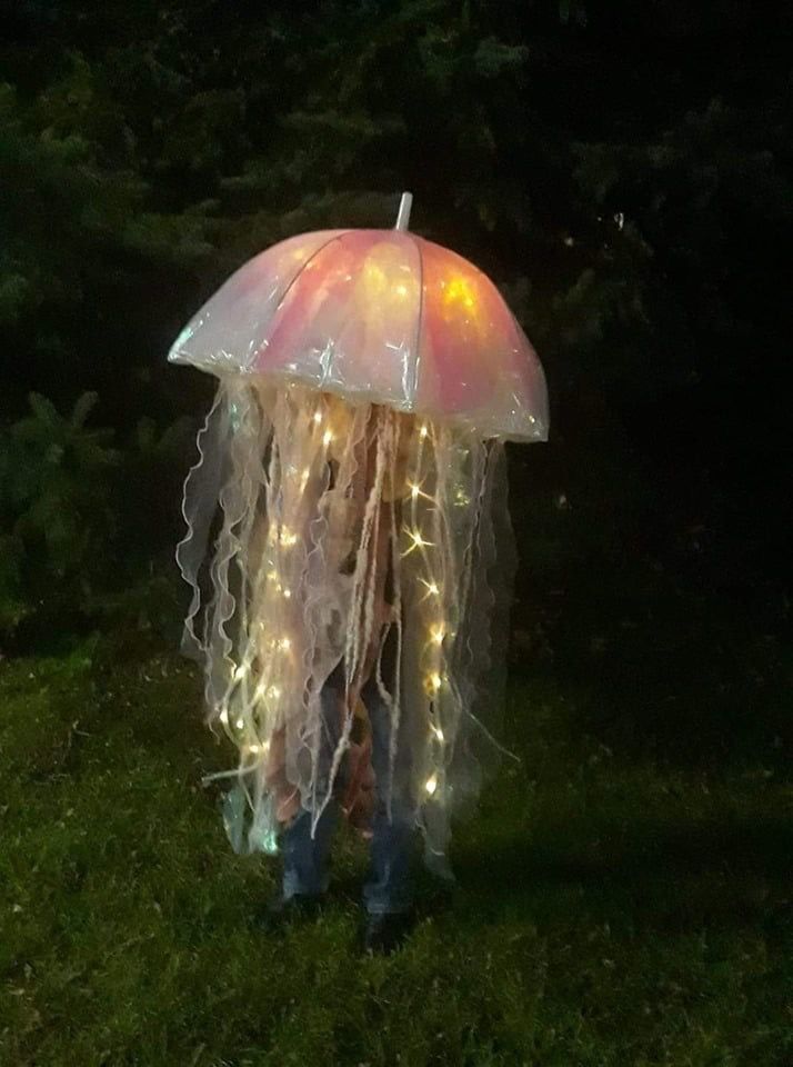 a jellyfish with lights on it's head is standing in the grass under an umbrella