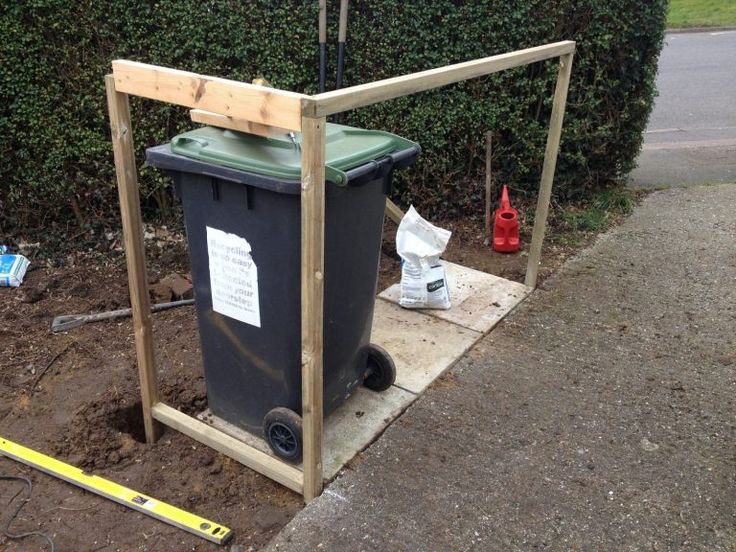 a trash can sitting on the side of a road next to a fence and bushes