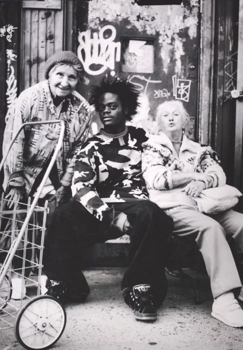 three people sitting on a bench in front of a building with graffiti all over it