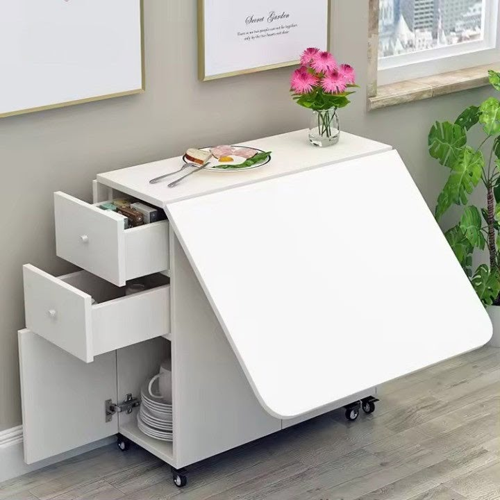 a white desk with drawers and flowers on it next to a potted plant in front of a window