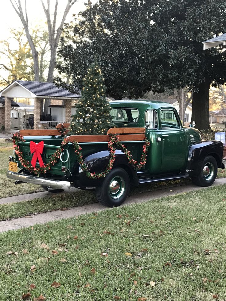 an old green truck with christmas decorations on the bed parked in front of a house