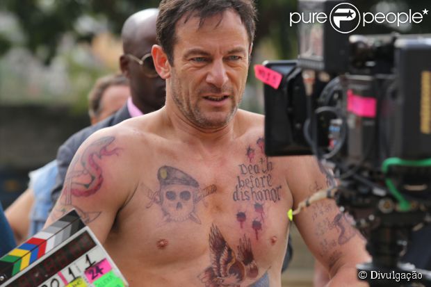 a shirtless man is holding a camera and looking at the camera with tattoos on his chest