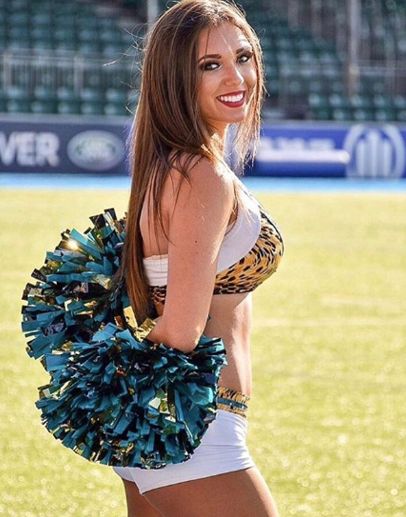 a beautiful young woman holding a cheerleader's pom - pom in front of a soccer field