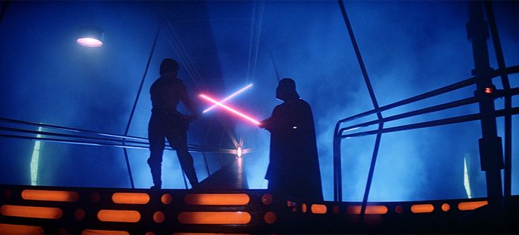 two people standing on top of a stage with lights in the background and one person holding a light saber