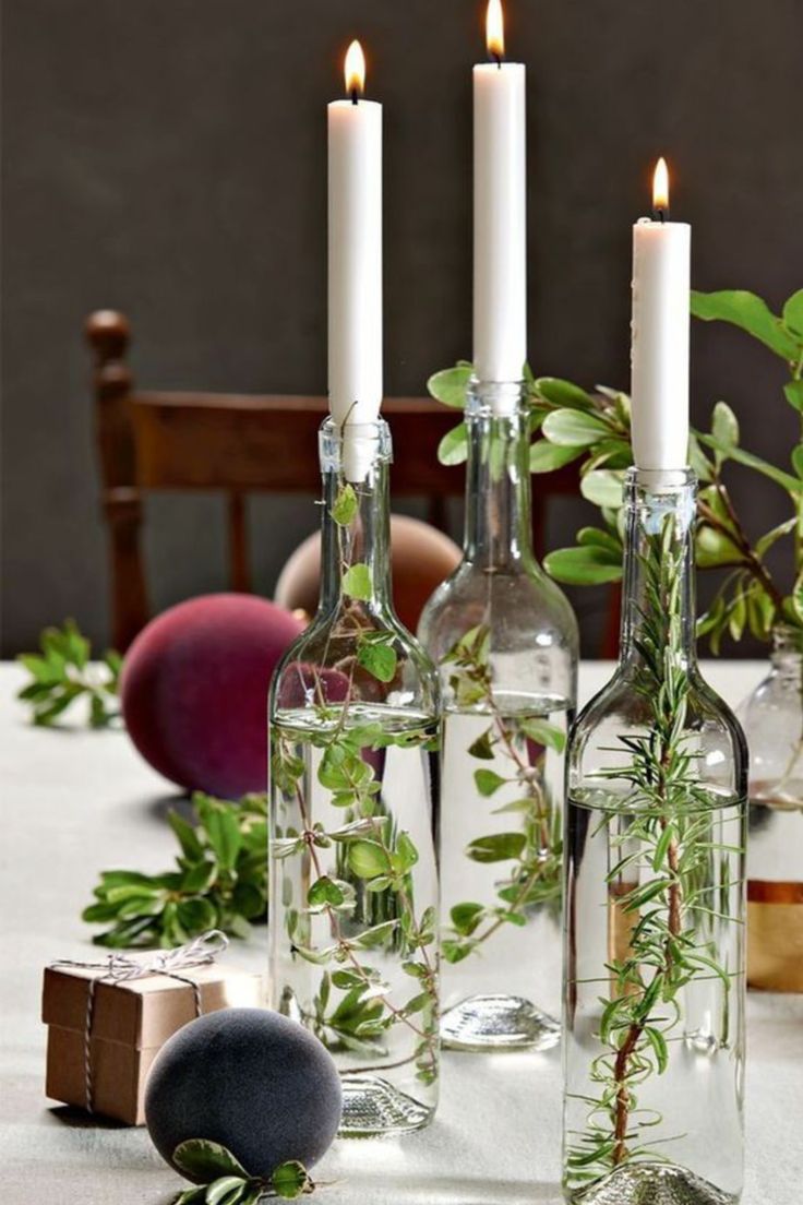 three bottles with plants in them sitting on a table next to rocks and candlesticks