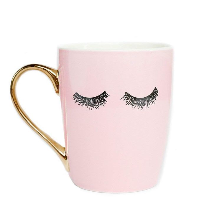 a pink coffee cup with eyelashes painted on the side and gold rimmed mug handle