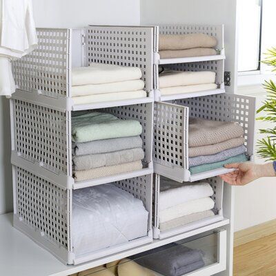 a person is holding up some folded towels in front of a shelf with baskets on it