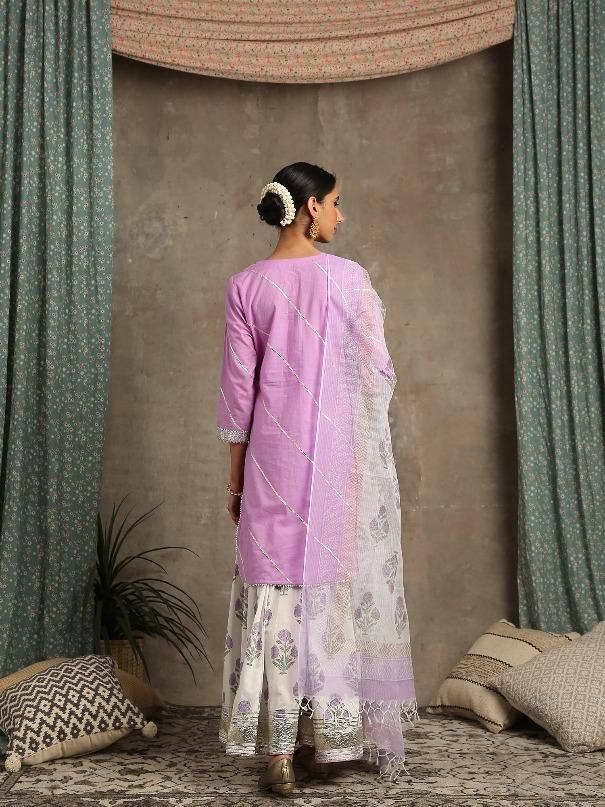 Set of 3 consists of kurta, dupatta and sharara. Kurta- U shape cotton kurta with lehriya gota work and bijiya detailing. Sharara- coton ghera sharara with hand printed poppies in soothing lavender. Detailed with lappa and handmade magzi at the ghera and joint of the sharara. Dupatta- Hand woven kota doriya dupatta. Colour - Ivory / Lavender Fabric - Cotton / Kota Doria Occasion - Festive Wear / Occasion Wear Fit - straight and flowy Pattern - Solid Care - Dry Clean only Estimated Delivery 15-20 Printed Salwar Suit, Gota Work, Cotton Kurta, Salwar Suit, Suit Set, Salwar Suits, Festival Wear, Occasion Wear, Printed Cotton