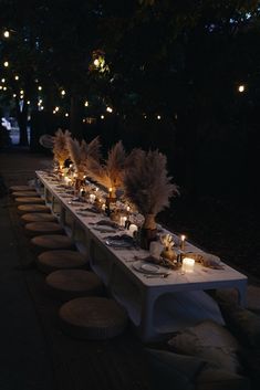 a long table set up with candles and flowers on it for an outdoor dinner party