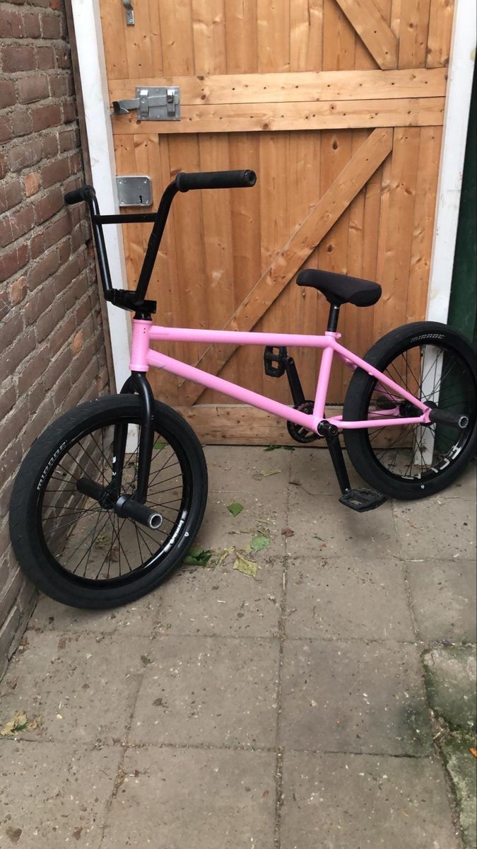 a pink bike parked in front of a wooden door with black rims on it