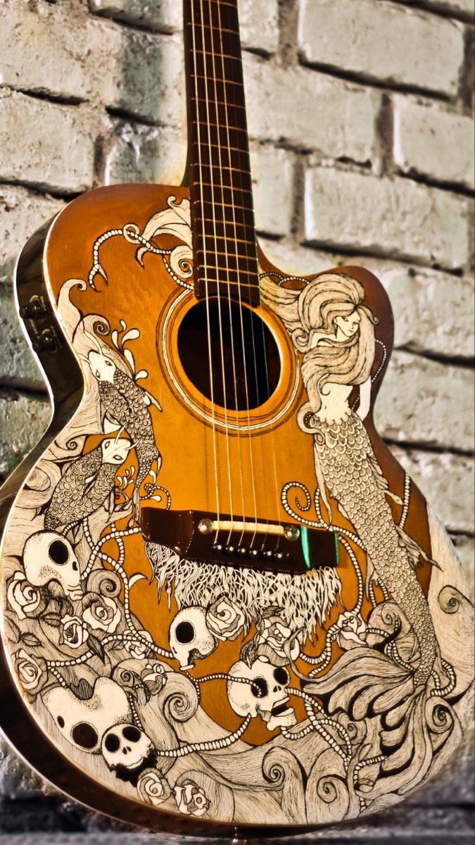 an acoustic guitar is decorated with skulls and mermaids