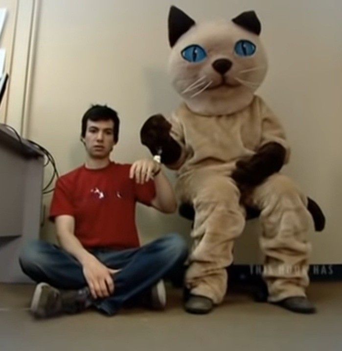 a man sitting on the ground next to a cat mascot