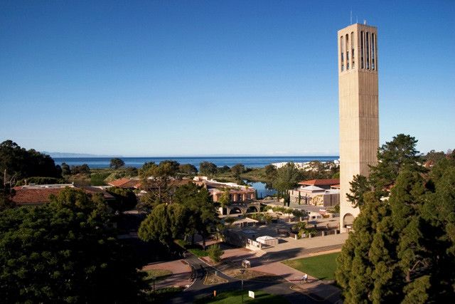 a tall tower with a clock on the side of it next to trees and water