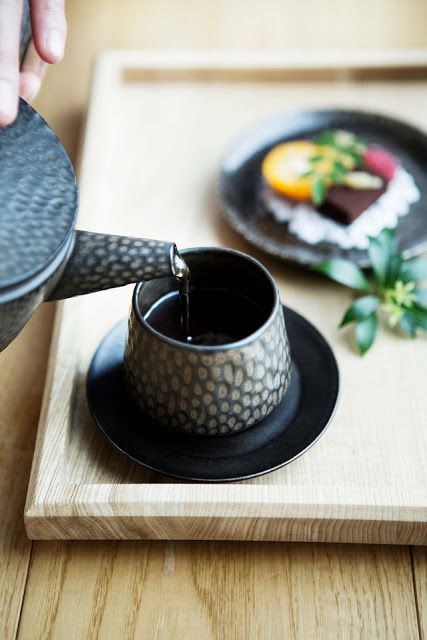 a person pours water into a cup on top of a wooden tray next to a plate