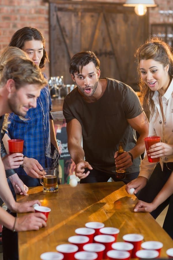 a group of people standing around a wooden table with cups in front of them and one person holding a drink