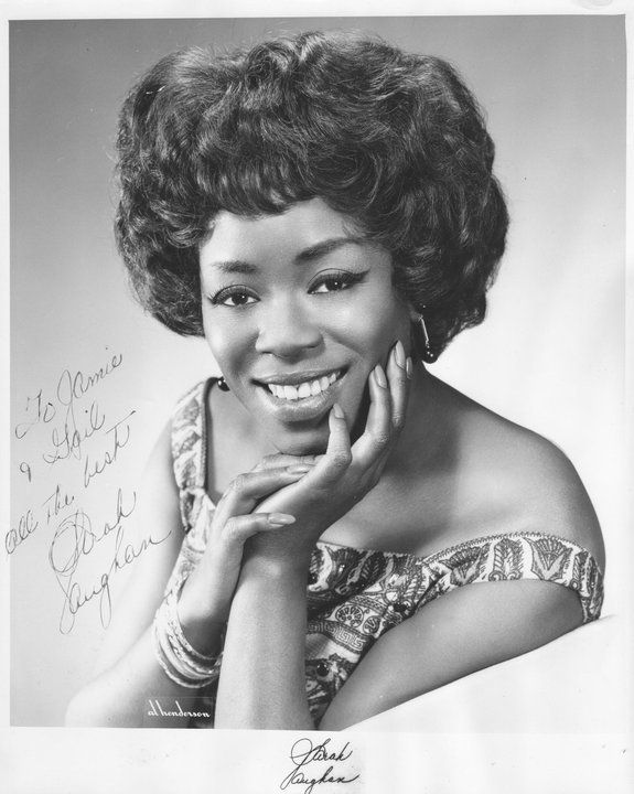 an old black and white photo of a woman with her hand on her chin, smiling