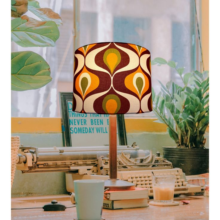 a lamp sitting on top of a wooden table next to a cup and plant in front of a window