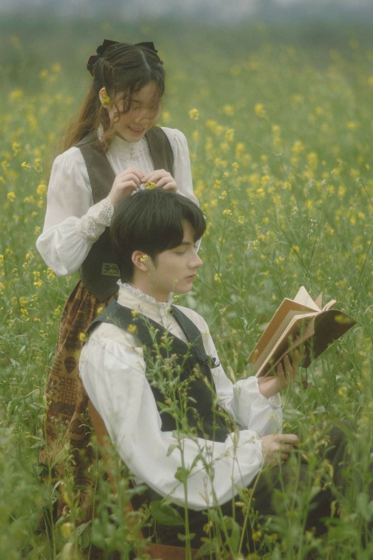 two people are sitting in the grass and one is reading a book while the other looks at something