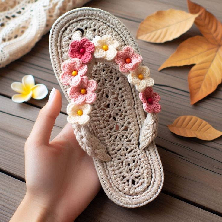 a person is holding up a crocheted slipper with flowers on the bottom