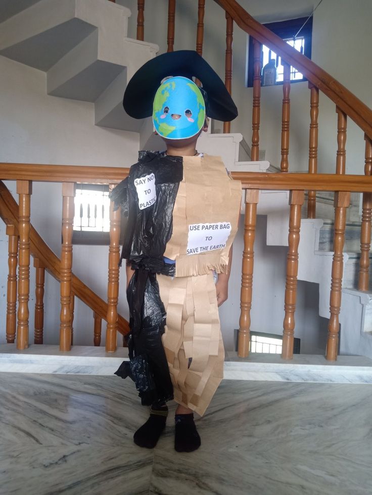 a child in a paper bag costume standing on the floor with a blue face and black hat