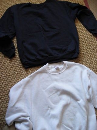 two black and white sweatshirts laying on the floor next to each other, one is unbuttoned