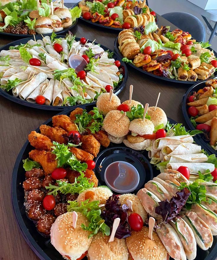 a table topped with lots of different types of sandwiches and salads on black plates