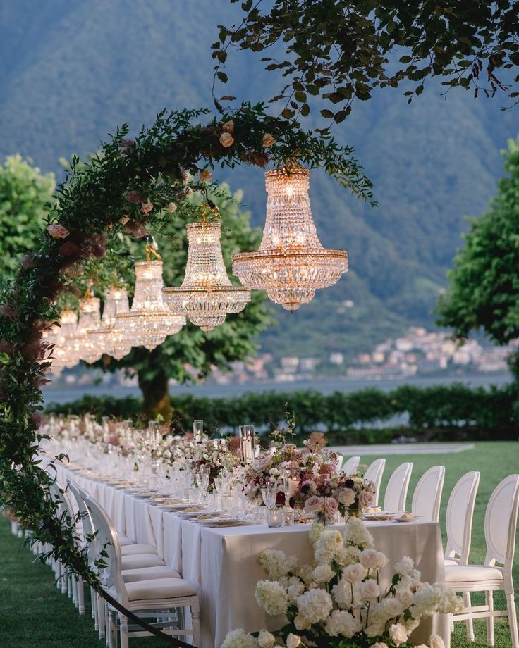 an outdoor dinner table with chandeliers and flowers