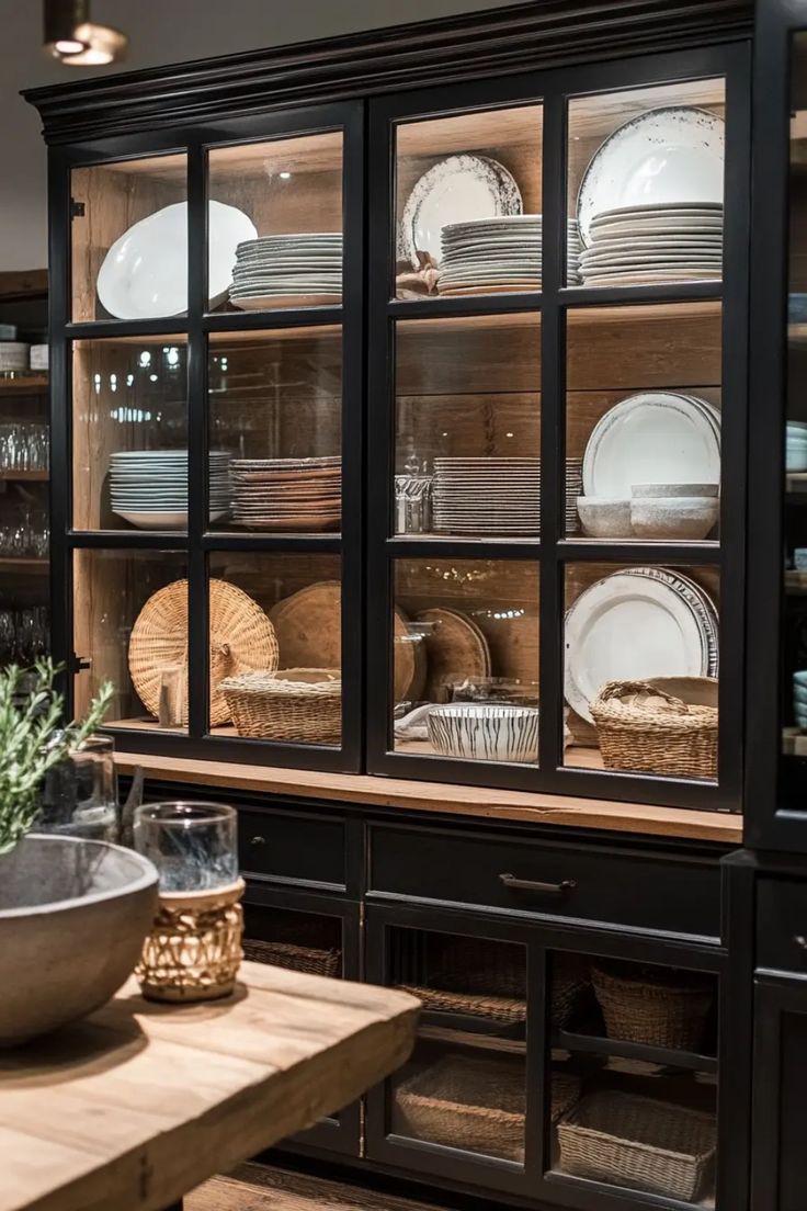 a wooden table topped with lots of plates and bowls next to a glass front cabinet