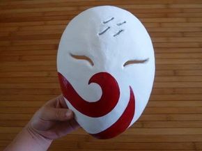 a person holding up a white mask with red swirls on it